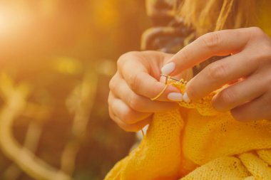 uzun sarı saçlı genç bir kız yaz aylarında bahçede sarı bir kazak örer. kadın elleri yakın ile giysi yapar