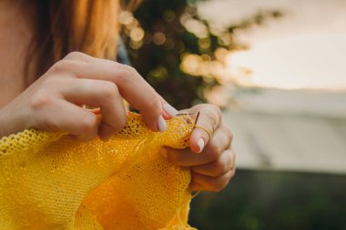 uzun sarı saçlı genç bir kız yaz aylarında bahçede sarı bir kazak örer. kadın elleri yakın ile giysi yapar