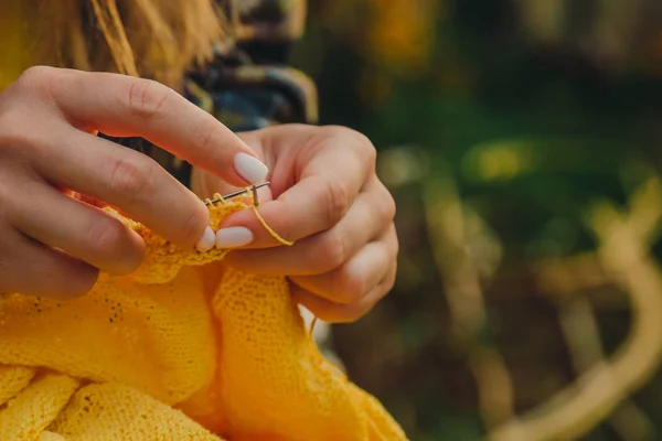 Une jeune fille aux longs cheveux blonds tricote un pull jaune dans le jardin en été. femme fait des vêtements avec les mains gros plan — Photo