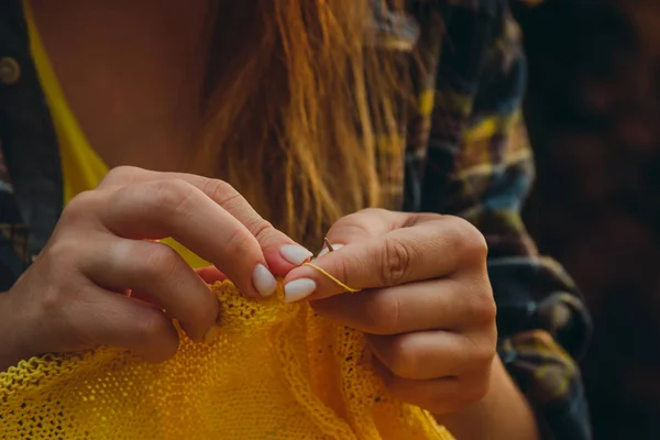 Une jeune fille aux longs cheveux blonds tricote un pull jaune dans le jardin en été. femme fait des vêtements avec les mains gros plan — Photo