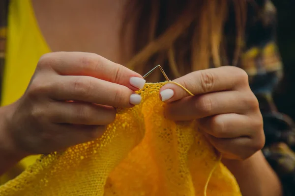 Een jong meisje met lang blond haar knits een gele trui in de tuin in de zomer. vrouw maakt kleren met handen close-up — Stockfoto
