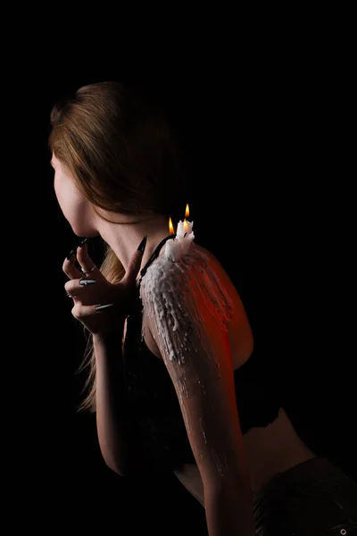 Ένα κορίτσι με μακριά μαλλιά στην εικόνα μιας μάγισσας προσπαθεί να βάλει φωτιά στον εαυτό της. τελετουργίες με κεριά για την αγάπη ξόρκι και τη ζημιά. απέλαση ενός κακού πνεύματος από το σώμα — Φωτογραφία Αρχείου
