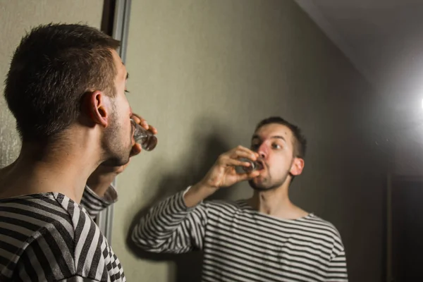 Een man die lijdt aan alcoholisme drinkt alleen thuis wodka, actie tegen alcohol. — Stockfoto