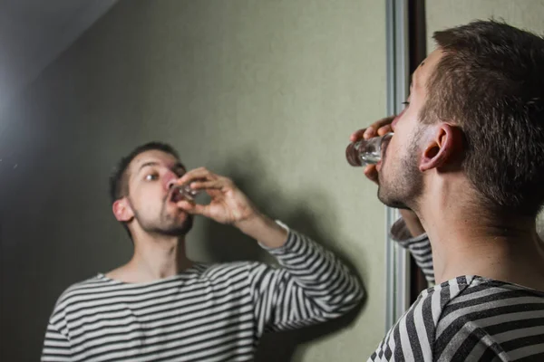 Een man die lijdt aan alcoholisme drinkt alleen thuis wodka, actie tegen alcohol. — Stockfoto