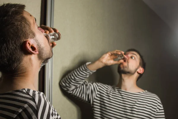 Een man die lijdt aan alcoholisme drinkt alleen thuis wodka, actie tegen alcohol. — Stockfoto