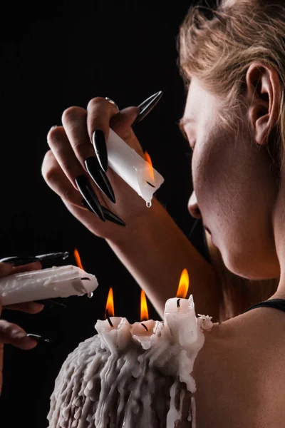 Ein Mädchen mit langen Haaren im Bild einer Hexe versucht, sich selbst in Brand zu setzen. Rituale mit Kerzen für Liebeszauber und Beschädigung. Vertreibung eines bösen Geistes aus dem Körper — Stockfoto