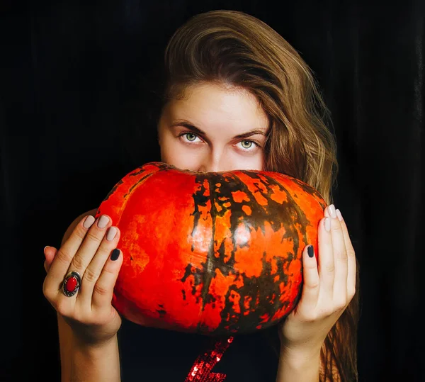 Ragazza con lunghi capelli biondi guarda scherzosamente tenendo una zucca tra le mani. concept photo per Halloween. su sfondo nero — Foto Stock