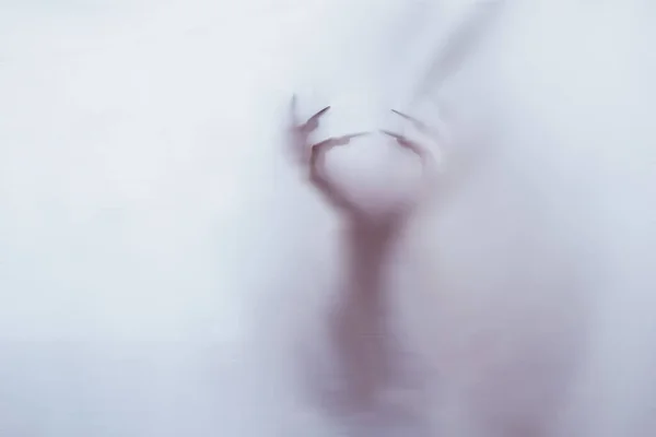 Silhueta de uma figura sexual feminina atrás de vidro nebuloso. conceito do espírito de poltergeist do outro mundo. mãos assustadoras da morte através do tecido . — Fotografia de Stock