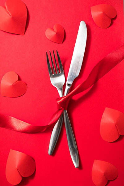 День святого Валентина романтическое свидание подготовка ужин со столовыми приборами, красная лента и сердца
