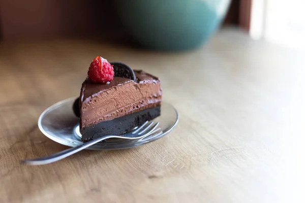 A piece of avocado chocolate vegan cake with oreo cookie and bright raspberry on top. Vegan desert.