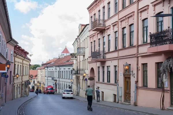 Ein Blick auf die Uzupio Straße in Uzupis, Vilnius, Litauen. Die Menschen nutzen grüne Verkehrsmittel: ein Fahrrad und einen Elektroroller. — Stockfoto