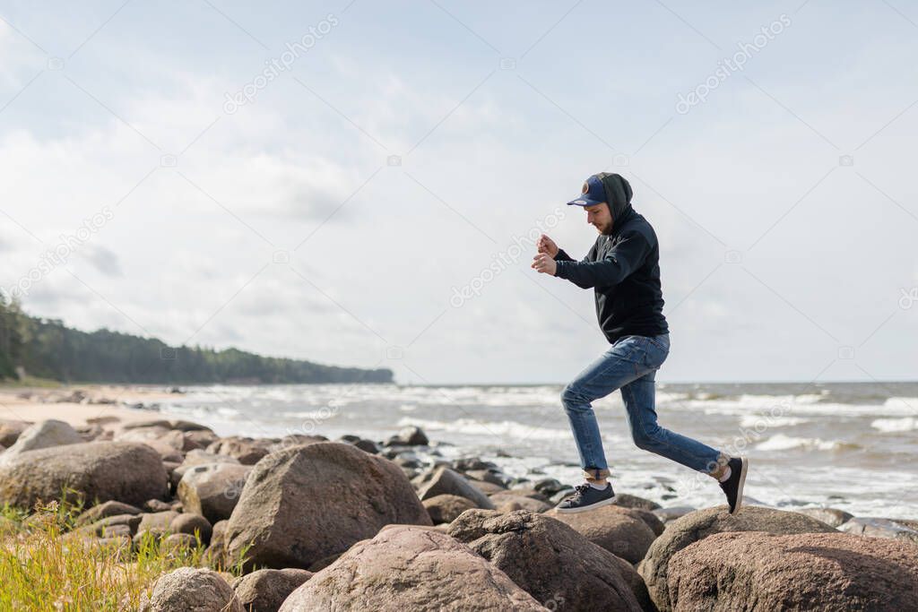 A young male having fun on the beachside of Baltic see, hopping from one large rock to another