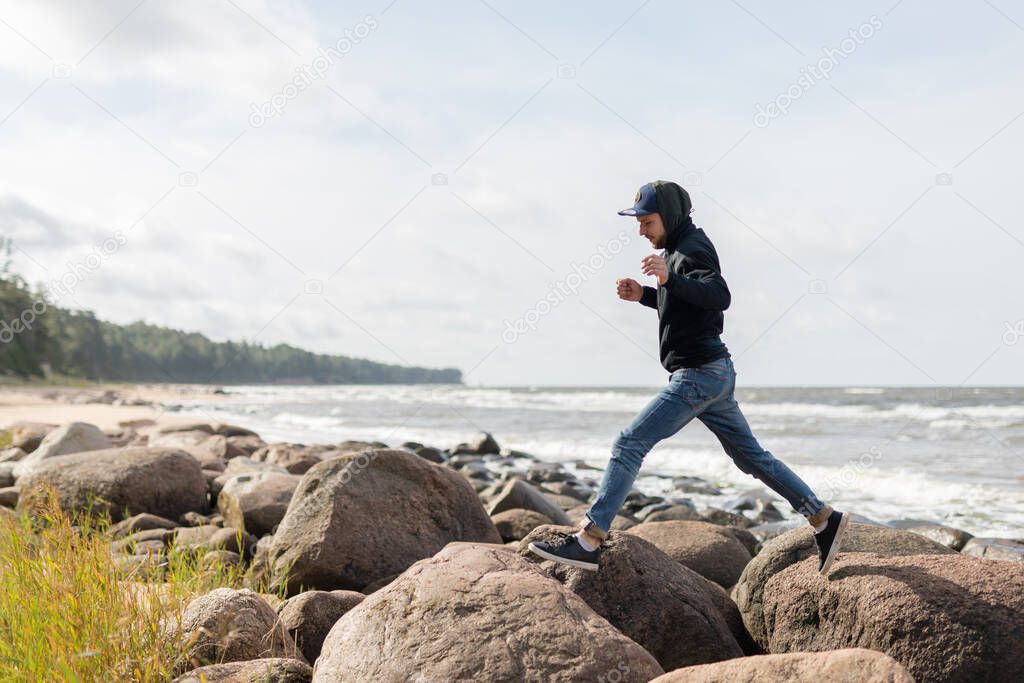 A young male having fun on the beachside of Baltic see, hopping from one large rock to another