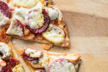 Dilimlenmiş salamlı pizza, mozzarella peyniri, beyaz mantar ve tahta kesme tahtasına konmuş Sriracha.