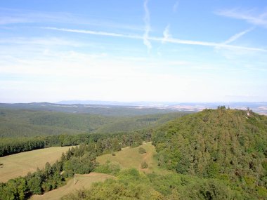 Tepeler yukarıdan görünüyor, küçük taretler, arka planda ormanlar, çayırlar, tarlalar, görüntüler var.