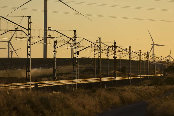 Train tracks superimposed on a landscape of silhouettes of operating wind turbines m in the Ribera Alta del ebro, in Aragon, Spain.