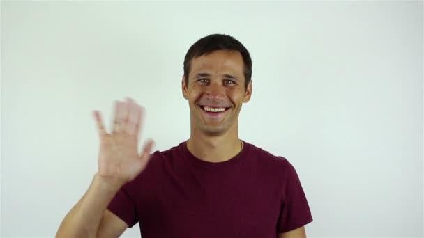 ビデオ チャットで話しながら 対談を歓迎ハンサムな若い男笑顔と彼の手を振って白い背景の上の肖像画 — ストック動画