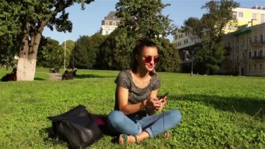 Güzel kız parkta çim üzerinde oturur ve onun favori melodi telefon kulaklık üzerinden dinler.