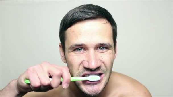 Young handsome guy brushing his teeth while looking into the camera. — Stock Video