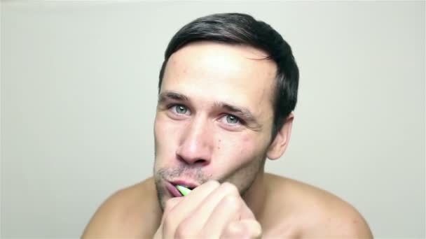 En ung, kjekk fyr som pusser tennene mens han ser inn i kameraet. . – stockvideo