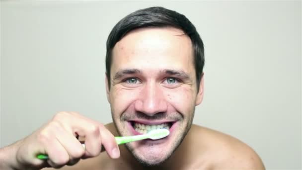 Junger gutaussehender Typ, der sich die Zähne putzt, lächelt und in die Kamera schaut. — Stockvideo