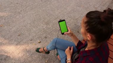 Sosyal ağlar parkta bir bankta oturmuş onu smartphone üzerinde leafing genç güzel kız.