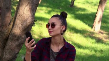 Bir bankta otururken genç güzel kız onun smartphone, şarkı söyler ve dans müzik dinler.