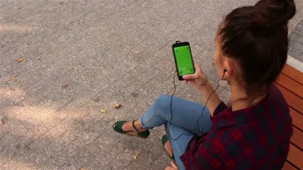 Молода красива дівчина залишає соціальні мережі на смартфоні, сидячи на лавці в парку . — стокове відео