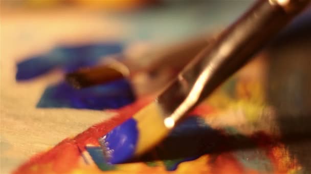 El artista sumerge el pincel en pintura azul mezclándolo en la paleta . — Vídeos de Stock