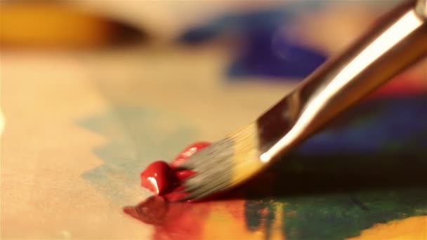 Artist lowers the brush in red paint and mixes it on the palette. — Stock Video