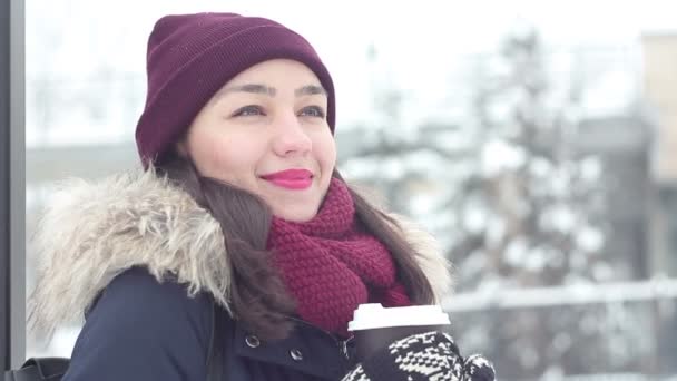 Piękna młoda dziewczyna wydmuchuje powietrze zimne powietrze, uśmiecha się i pije kawę z kubka w winter park. — Wideo stockowe