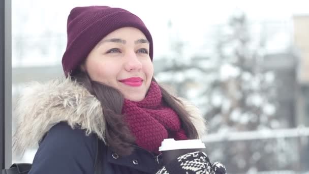 Schönes junges Mädchen atmet kalte Luft aus, lächelt und trinkt Kaffee aus einer Tasse im Winterpark. — Stockvideo