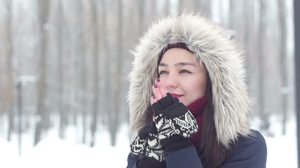 Vacker ung flicka värmer händerna med sin andetag medan promenader i skogen vinter. — Stockvideo