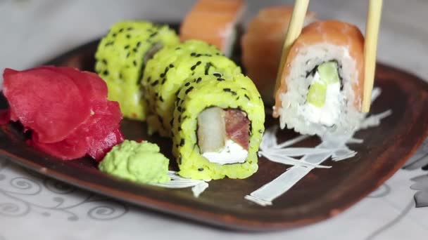 Χέρι με chopsticks βάζει ρολά σούσι σε ένα πιάτο και παίρνει τζίντζερ. — Αρχείο Βίντεο
