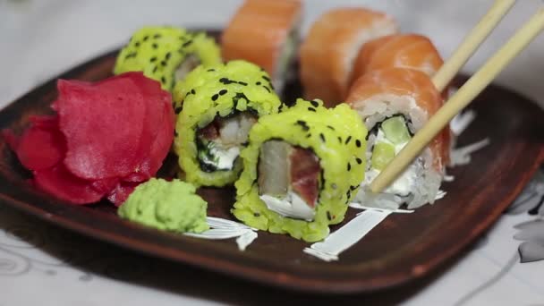 Рука с палочками для еды берет суши с тарелки. — стоковое видео