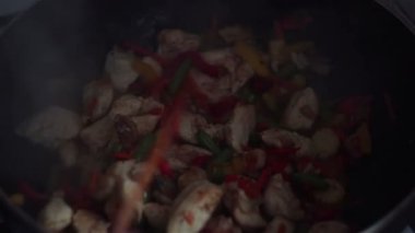 Şef bir tavuk ve sebze tabağı bir wok tavada tahta bir spatula ile karışımları