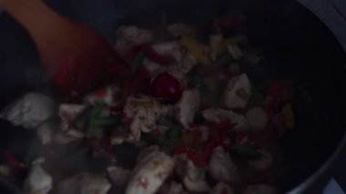 Şef bir tavuk ve sebze tabağı bir wok tavada tahta bir spatula ile karışımları