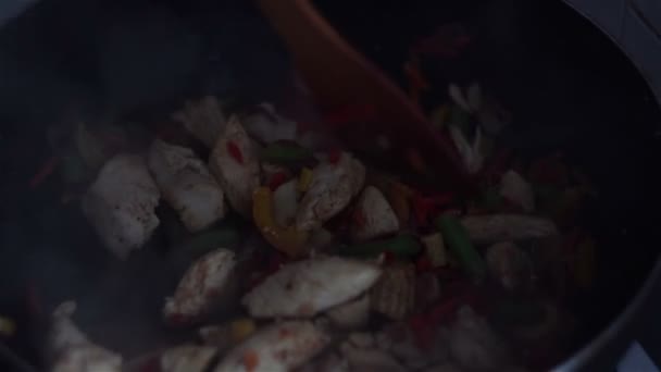 Chef mélange un plat de poulet et de légumes dans une casserole wok avec une spatule en bois — Video