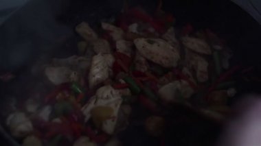 Şef bir tavuk ve sebze tabağı bir wok tavada tahta bir spatula ile karışımları