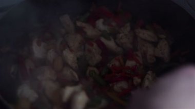 Şef bir tavuk ve sebze tabağı bir wok tavada tahta bir spatula ile karışımları