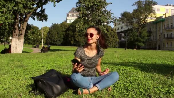 Bela Menina Sorridente Sentado Grama Parque Uma Tarde Ensolarada Ouvir — Vídeo de Stock