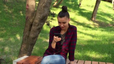 Genç kız güzel güneşli bir gün aktif Internet sohbet yeniden parkta bir bankta oturur.