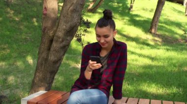 Genç güzel kız ekose gömlekli aktif Internet sohbet yeniden parkta bir bankta oturur