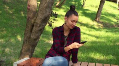 Genç güzel kız bir ekose gömlek gülümseyen ve onun smartphone içinde sosyal ağların teyp tarama.