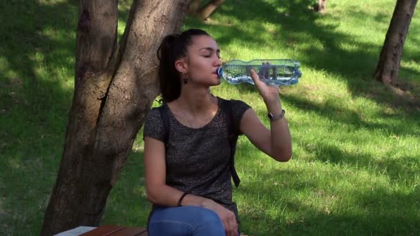 Young beautiful girl opens a plastic bottle with water and drinks water from her. — Stock Video