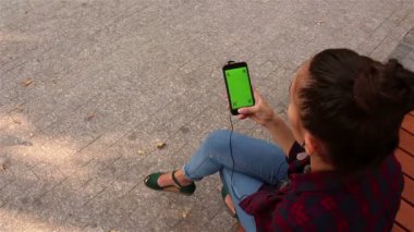Genç güzel kız onun smartphone cep telefonu ile parkta bir bankta oturmuş, müzik dinlemek.