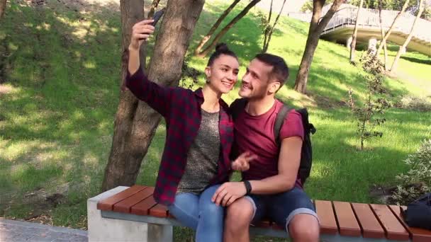 Молода закохана пара фотографується сидячи на лавці в парку . — стокове відео