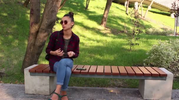 Unga älskande par, på en solig dag, gäspningar medan du sitter på en bänk i en park. — Stockvideo