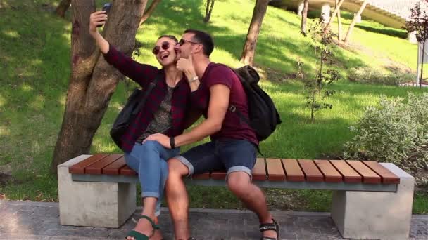 Молода закохана пара фотографується сидячи на лавці в парку. Вони посміхаються і обіймають один одного . — стокове відео