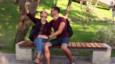 Aşık genç çift parkta bir bankta oturmuş fotoğraflandı. Gülümseyen ve birbirlerine sarılma.